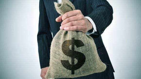 torso of man in suit holding out a stuffed burlap bag with a dollar sign on it